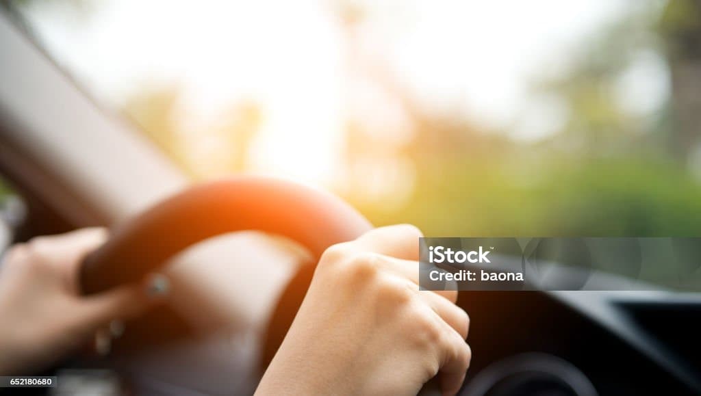 Close-up of hands gripping a steering wheel, driving during a sunny day. The background is blurred, suggesting movement and a sense of calm focus.